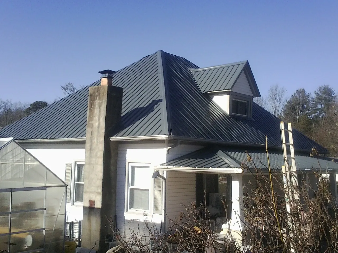 Dark blue standing seam metal roof on a white farmhouse with dormer — Slate & Tile Roof Repair by Roofing Brothers in Willoughby