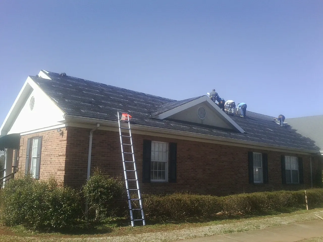 Crew tearing shingles off a brick ranch roof with a ladder set — Emergency Roof Repair work by our crew in Willoughby