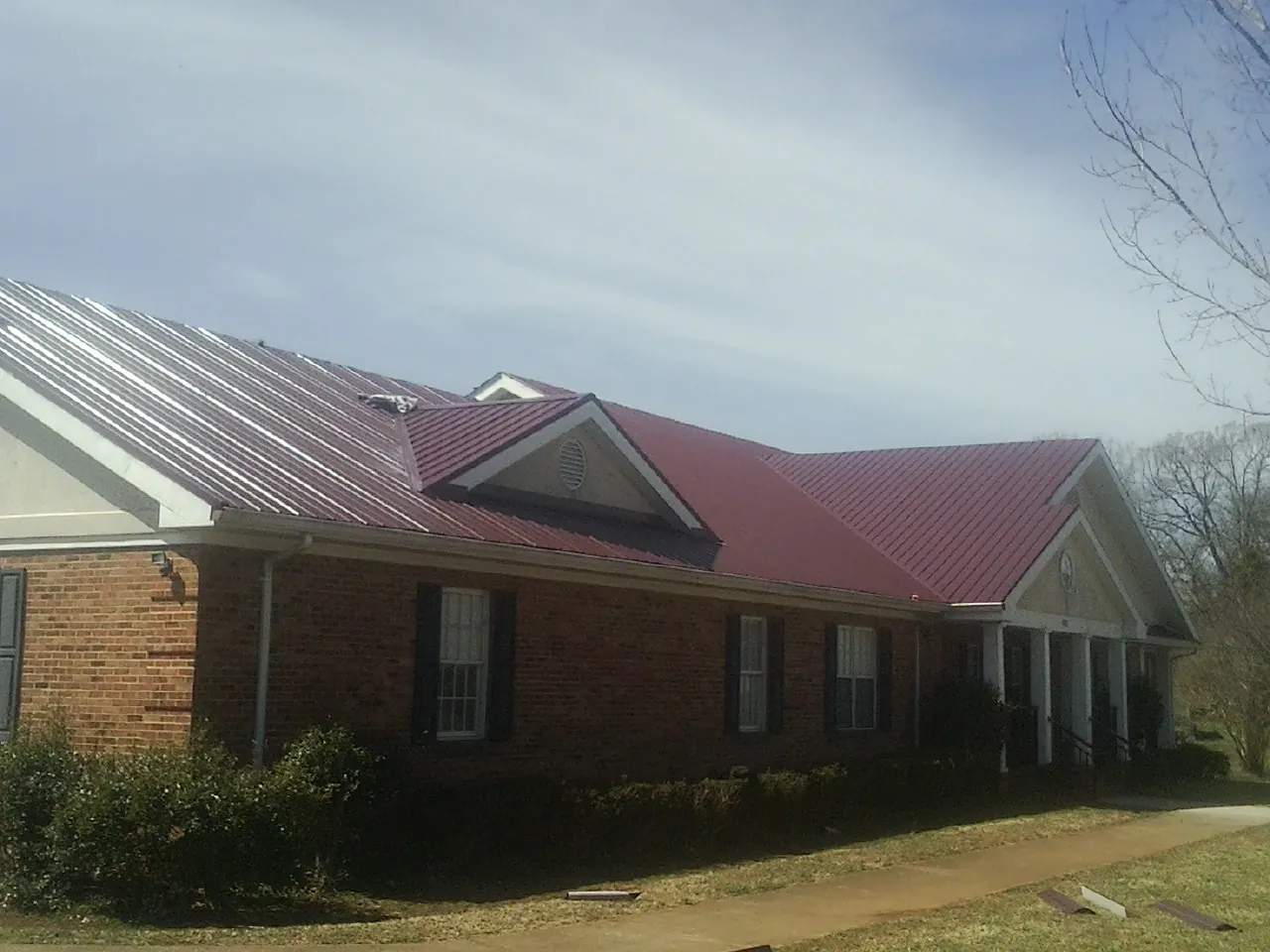Red metal roof with gabled entries on a long brick building, from a Hail Damage Roof Repair job in Willoughby