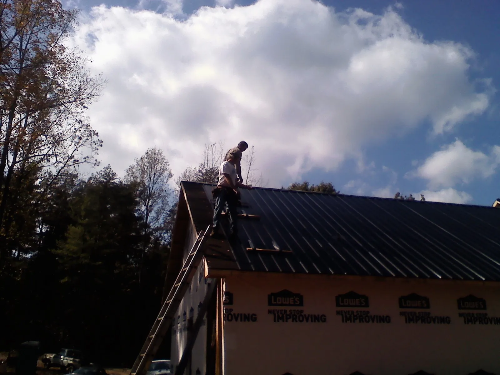 Roofer fastening dark metal panels high against a cloudy sky, from a Roof Inspection job in Willoughby