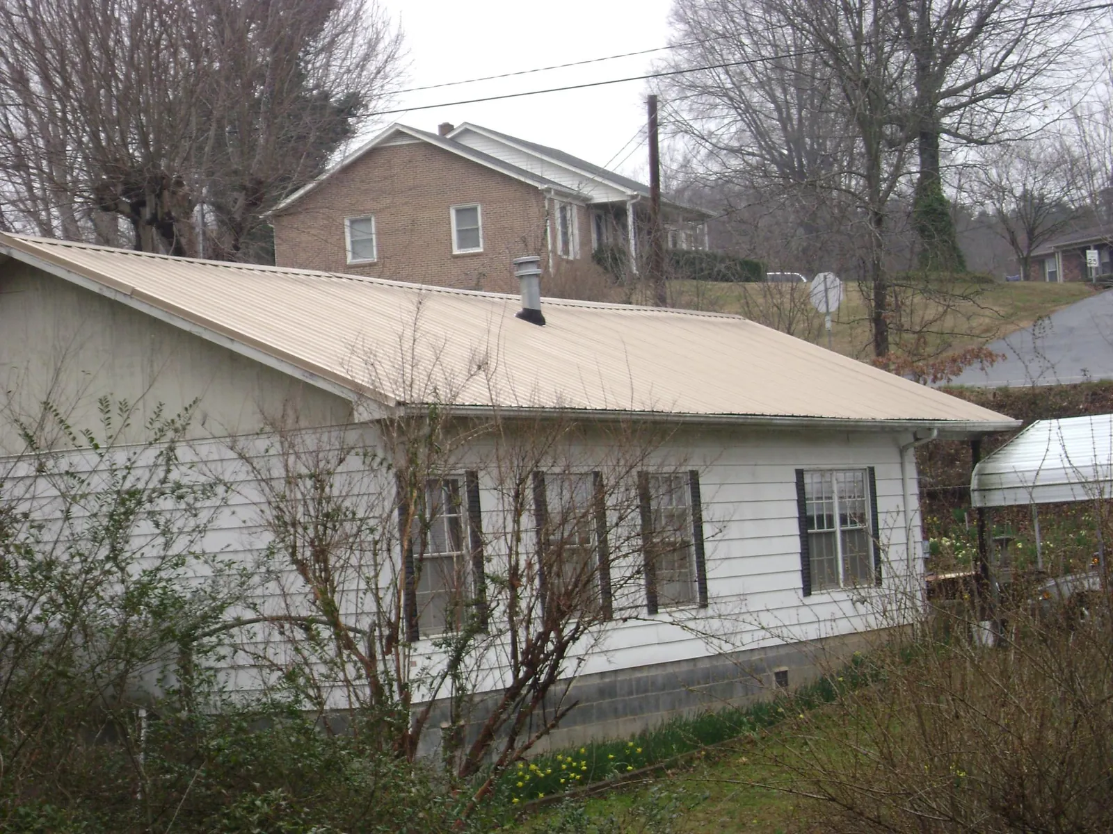 Tan metal roof on a white sided house set into a hillside — Commercial Roofing by Roofing Brothers in Willoughby